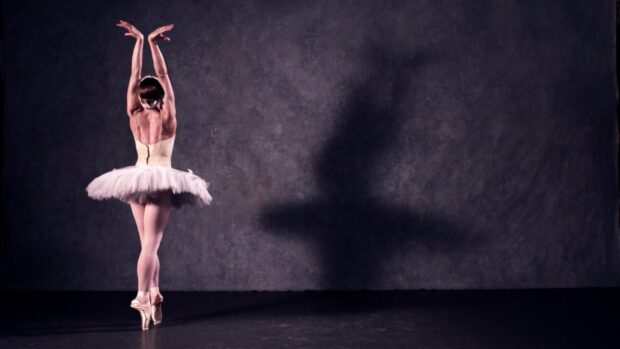 A ballet dancer is standing on pointe with arms raised creating a shadow, HD Desktop Wallpaper