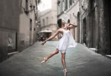 A ballet dancer is performing an elegant pose while wearing a white dress on a cobblestone street, HD Desktop Wallpaper
