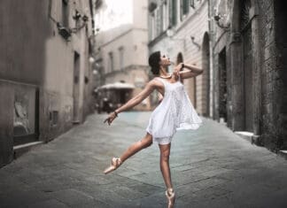 A ballet dancer is performing an elegant pose while wearing a white dress on a cobblestone street, HD Desktop Wallpaper