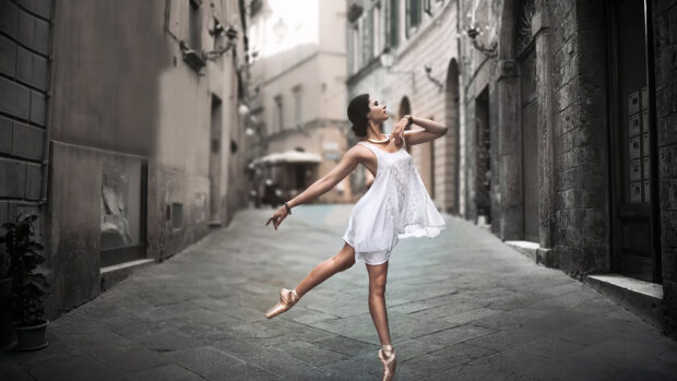 A ballet dancer is performing an elegant pose while wearing a white dress on a cobblestone street, HD Desktop Wallpaper