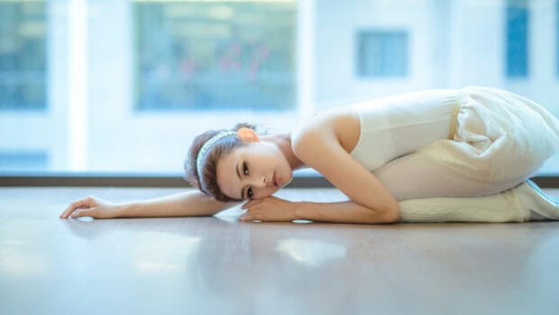 A ballet dancer in a white outfit is resting on a wooden floor near a window with blue light, HD Desktop Wallpaper