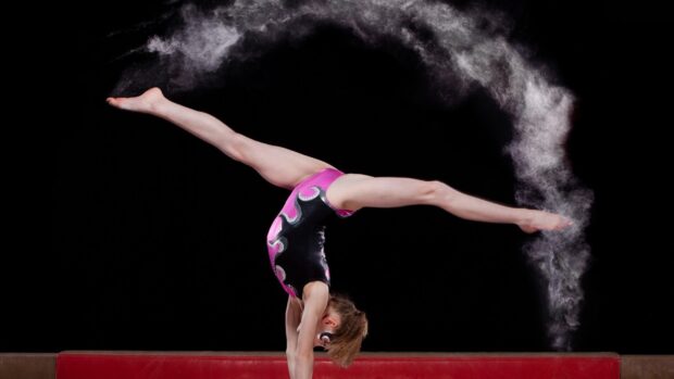 A gymnast performs a split handstand on a balance beam with chalk dust, HD Desktop Wallpaper