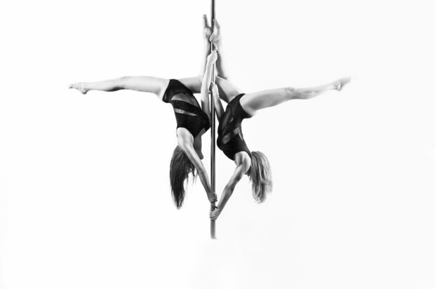 Two women performing a synchronized pole dance routine showcasing strength and balance, HD Desktop Wallpaper