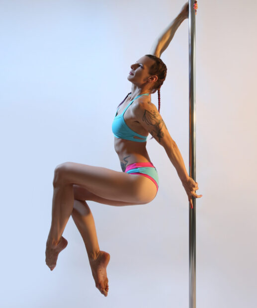 A fit woman with tattoos performs a graceful pole dance pose with strength and balance, 2K Mobile Wallpaper