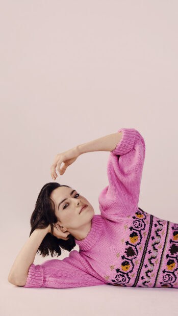A graceful portrait of Daisy Ridley wearing a pink knitted sweater while reclining against a soft background, 4K Mobile Wallpaper