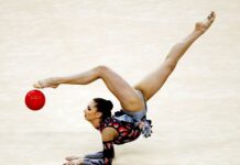 A rhythmic gymnast is captured balancing on her arms while lifting legs in an elegant pose with a red ball, HD Desktop Wallpaper