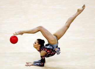 A rhythmic gymnast is captured balancing on her arms while lifting legs in an elegant pose with a red ball, HD Desktop Wallpaper