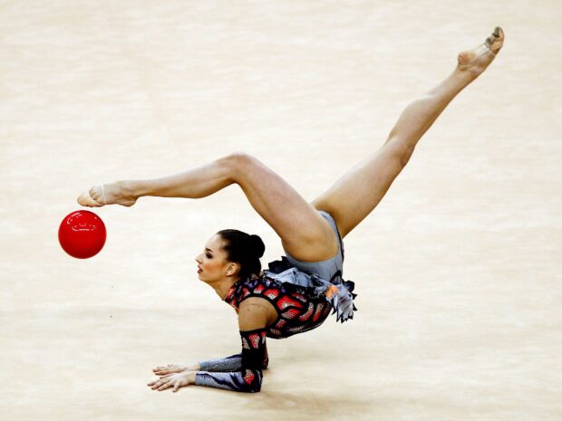A rhythmic gymnast is captured balancing on her arms while lifting legs in an elegant pose with a red ball, HD Desktop Wallpaper