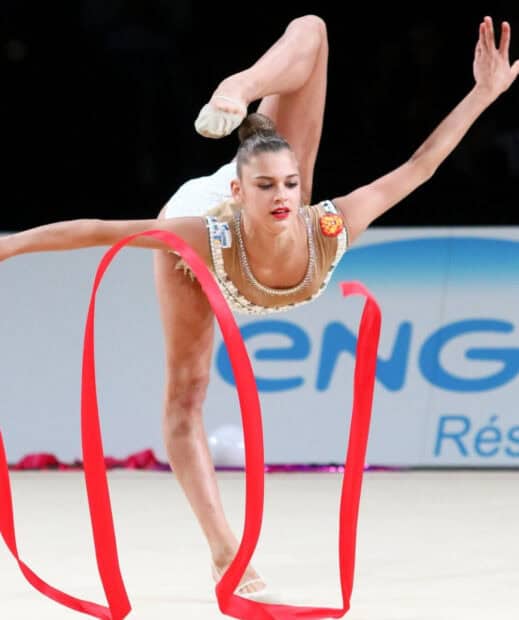 A rhythmic gymnast is captured in a balancing pose while performing with a red ribbon, HD Mobile Wallpaper
