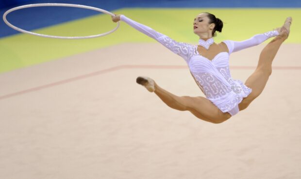A rhythmic gymnastics athlete performs an elegant leap holding a hoop during competition, HD Desktop Wallpaper