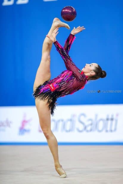 A rhythmic gymnast performs a high leg lift while balancing a ball during a competition, HD Mobile Wallpaper