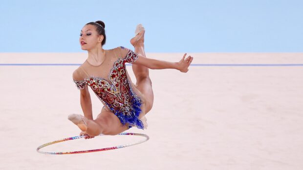 A rhythmic gymnastics athlete performs a leap while holding a hoop during competition, HD Desktop Wallpaper