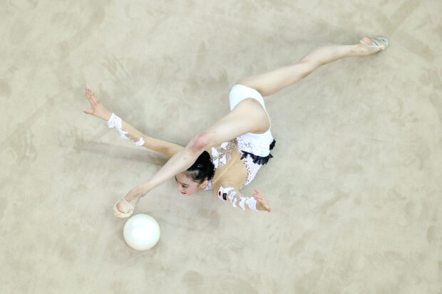 A rhythmic gymnastics athlete stretches on the floor with a ball during her routine, HD Desktop Wallpaper