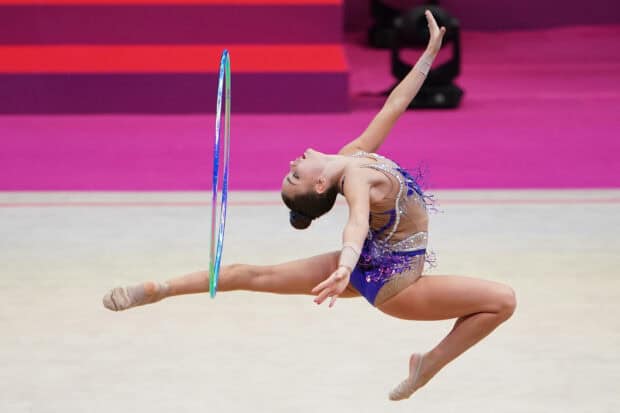 A graceful rhythmic gymnast leaps with a hoop in midair during a competition, HD Desktop Wallpaper