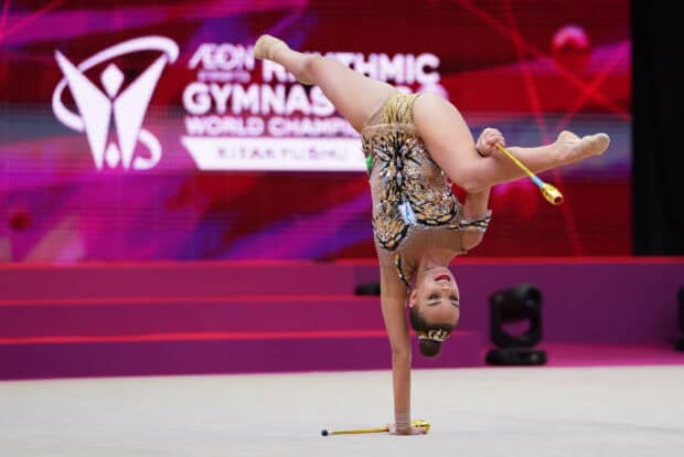A rhythmic gymnast balances on one hand while performing with golden clubs, HD Desktop Wallpaper