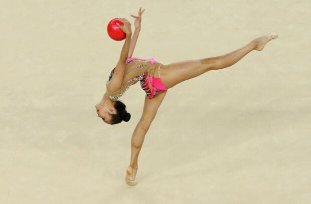 A gymnast performs a flexible pose while holding a red ball during rhythmic gymnastics, 2K Desktop Wallpaper