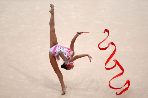 A rhythmic gymnast performs a split leap while twirling a red ribbon, HD Desktop Wallpaper
