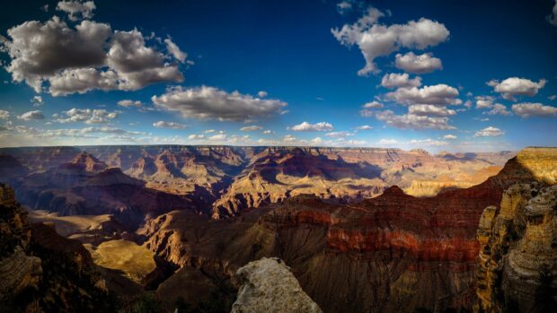 A panoramic view of the Grand Canyon with vivid red rocks and scattered clouds in the blue sky, 4K Desktop Wallpaper