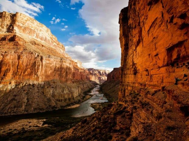 The Grand Canyon displays a river winding through towering red rock cliffs under a partly cloudy sky, 2K Desktop Wallpaper
