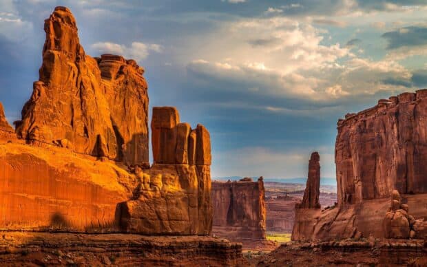 The Grand Canyon rock formations glow with warm sunlight under a partly cloudy sky, 2K Desktop Wallpaper