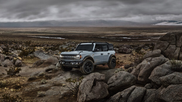 A gray Ford Bronco is driving off road over rocky terrain with a cloudy sky, 4K Desktop Wallpaper