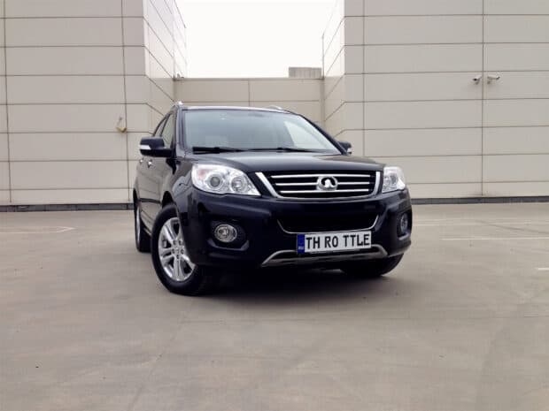 A black Great Wall Motors SUV is parked on a concrete surface near modern white buildings, HD Desktop Wallpaper