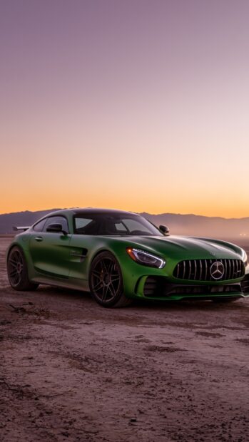 A green Mercedes Benz AMG GT is parked on a dirt surface with a mountain range in the background during sunset, HD Phone Wallpaper