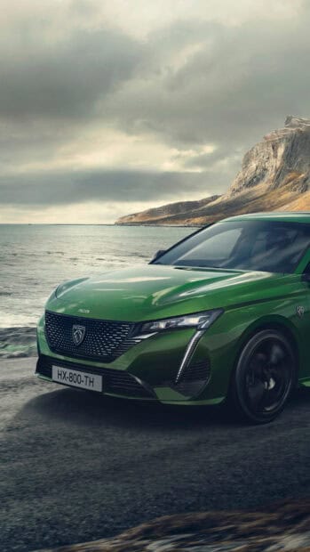 A green Peugeot 308 drives along a coastal road with rocky cliffs and cloudy sky in the background, 4K Phone Wallpaper