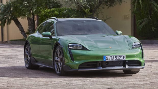 A green Porsche Taycan is parked outside with surrounding plants and clear skies, 4K Desktop Wallpaper