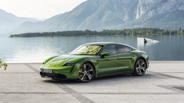 A green Porsche Taycan stands on a paved area beside a serene lake with mountains in the background, HD Desktop Wallpaper