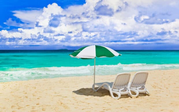 A green and white beach umbrella stands between two lounge chairs on a sandy beach near the turquoise ocean, 2K Desktop Wallpaper
