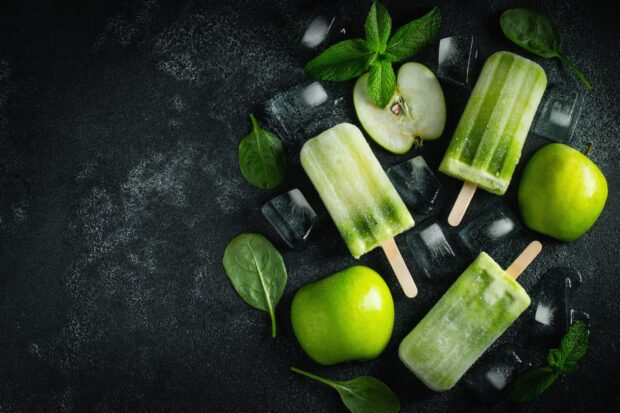 A close up of green apple popsicles surrounded by mint leaves and ice cubes on a dark surface, 2K Desktop Wallpaper