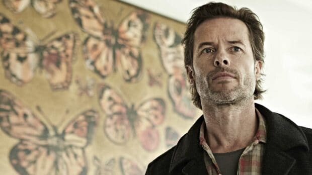 A close up of Guy Pearce with a butterfly painting behind him, 2K Desktop Wallpaper
