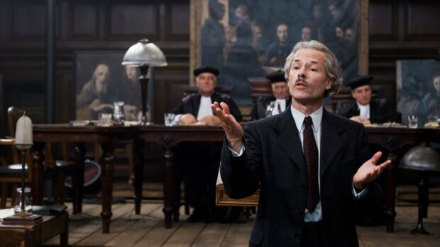 Guy Pearce is shown speaking confidently during a courtroom scene with judges in the background