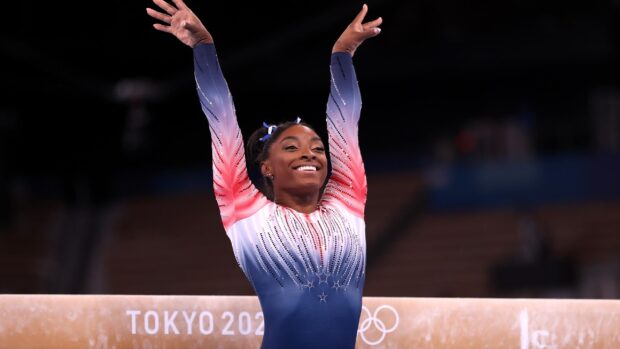 A gymnast is smiling confidently during a balance beam routine with a Tokyo 2020 background, 2K Desktop Wallpaper