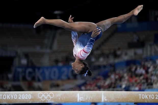 A gymnast is executing a complex flip on the balance beam during the competition, HD Desktop Wallpaper