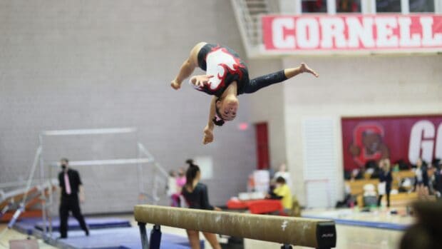 A gymnast is performing a mid air flip above the balance beam during a competition, HD Desktop Wallpaper
