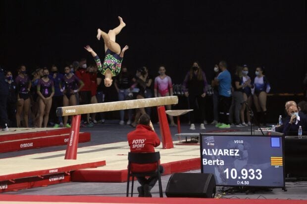 A gymnast is captured mid flip on the balance beam during a competition, HD Desktop Wallpaper