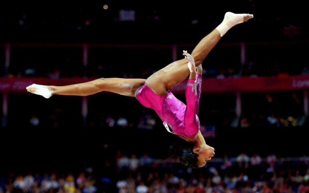 A gymnast executes a precise aerial move on the balance beam during a competition, HD Desktop Wallpaper
