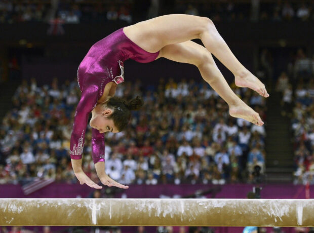 A gymnast performs a precise acrobatic gymnastics routine on a balance beam in front of a crowd, 2K Desktop Wallpaper