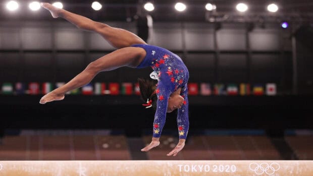 A gymnast is captured mid air above the balance beam during an Olympic event, HD Desktop Wallpaper