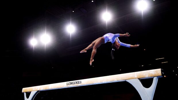 A gymnast is captured mid air above the balance beam during a gymnastics competition, HD Desktop Wallpaper