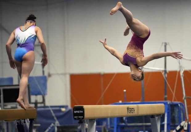 Two female gymnasts practicing skills on the balance beam in a gym, HD Desktop Wallpaper