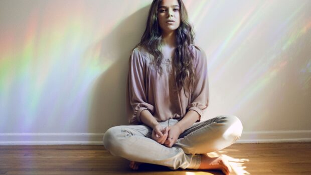 Hailee Steinfeld is sitting cross legged against a wall with colorful light reflections, HD Desktop Wallpaper