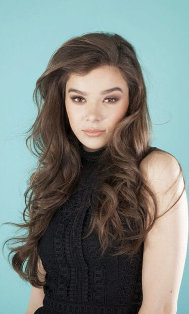A close up of Hailee Steinfeld wearing a black dress with long wavy hair against a blue background, HD Phone Wallpaper