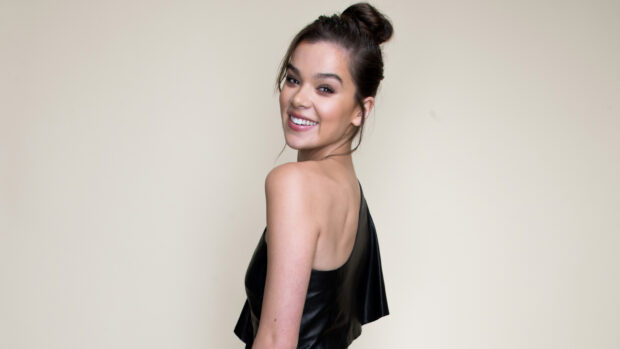 Hailee Steinfeld is smiling while posing against a plain beige background, 2K Desktop Wallpaper