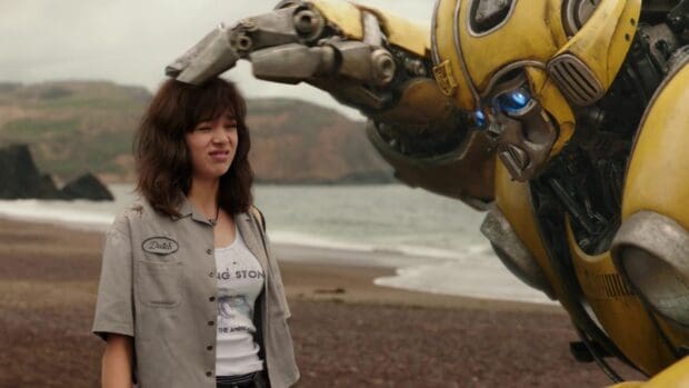 Hailee Steinfeld stands next to a large yellow robot on a rocky beach, HD Desktop Wallpaper