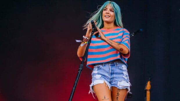 A female artist with blue hair is performing live on stage holding a microphone stand in a concert, HD Desktop Wallpaper