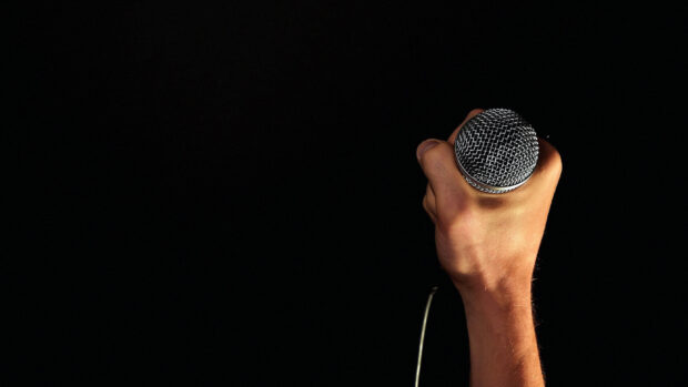 A hand firmly holding a microphone against a black background for microphone wallpapers, 4K Desktop Wallpaper