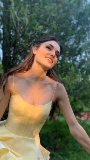 Hande Ercel is smiling outdoors wearing a yellow dress with greenery in the background, HD Phone Wallpaper